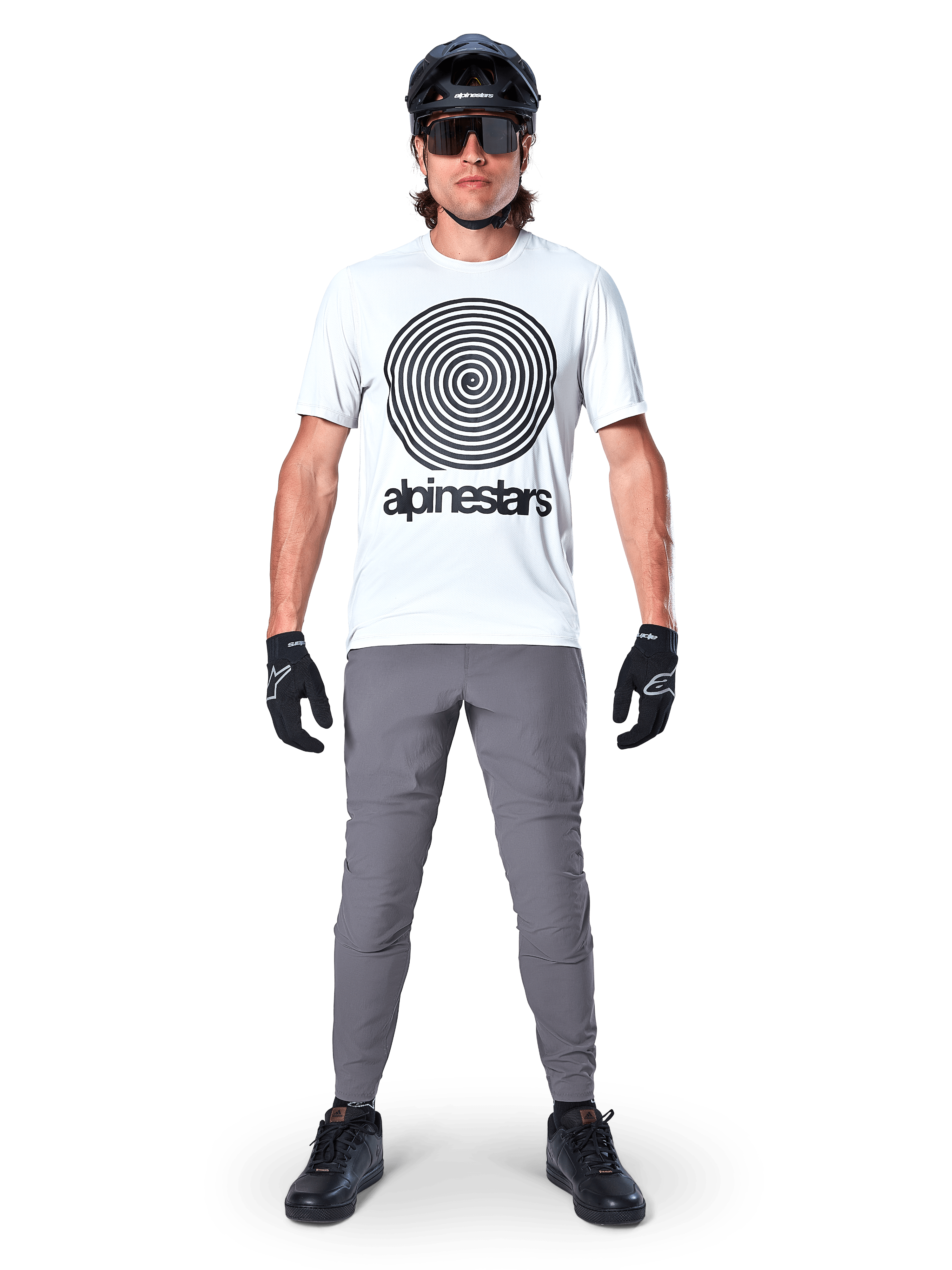 Calças Alpinestars A-Dura, calças de ciclismo MTB, cinza escuro, usadas com t-shirt branca com grafismo, capacete e luvas pretos, com design durável de elasticidade bidirecional e ajuste regular para mountain bike