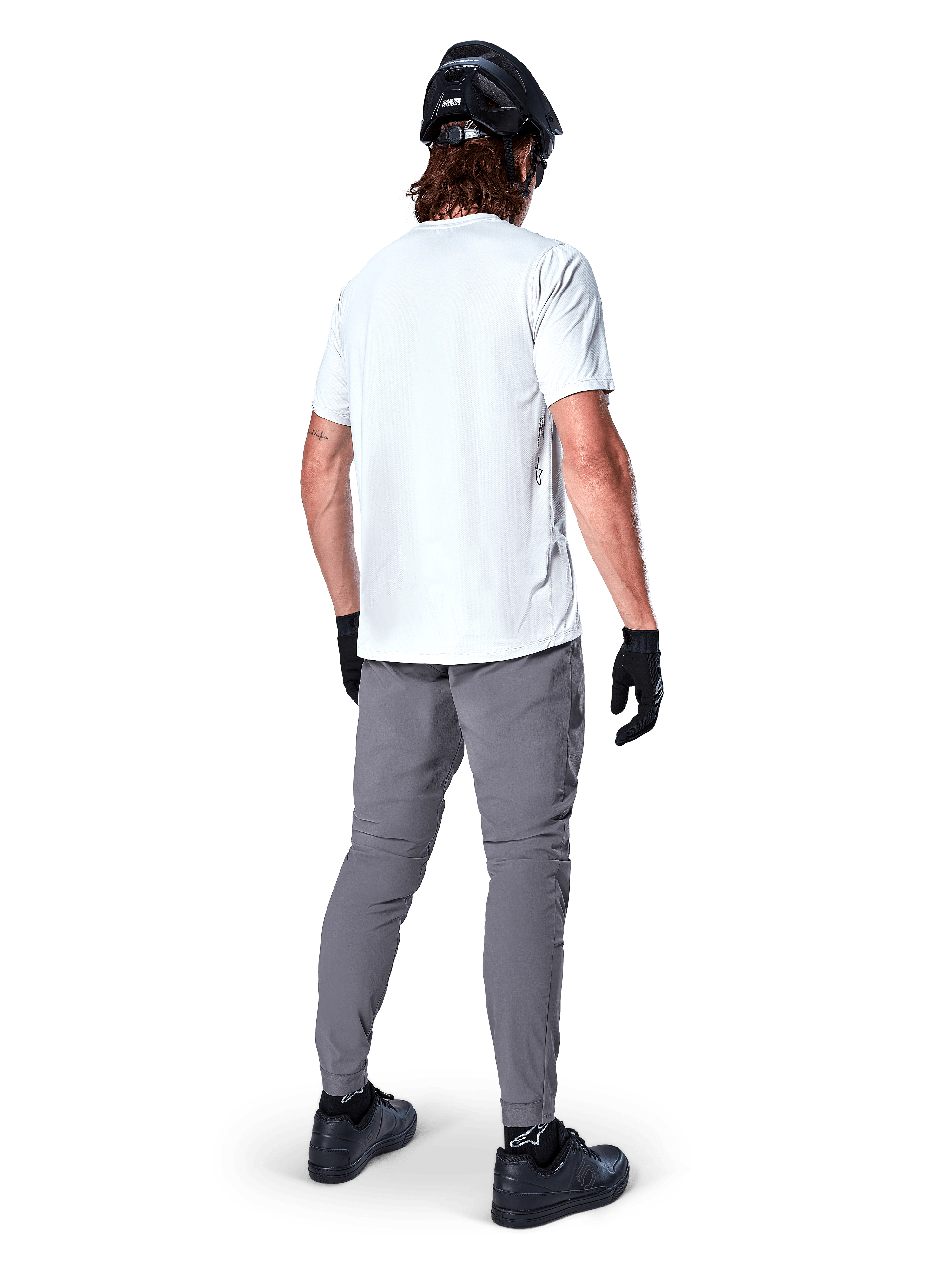 Calças Alpinestars A-Dura, calças de BTT em cinzento escuro vistas de trás, usadas com uma t-shirt branca de manga curta, capacete de BTT preto, luvas e sapatos pretos, design de corte regular com punhos elásticos, equipamento de ciclismo todo-o-terreno durável
