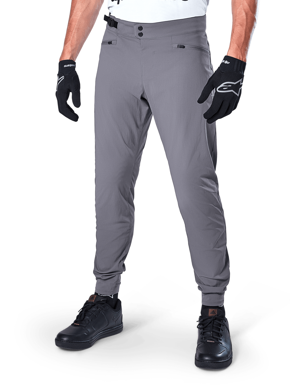 Calças Alpinestars A-Dura, calças de MTB cinzento escuro, com fecho de pressão duplo na cintura e bolsos com fecho de correr, punhos elásticos, usadas com luvas de ciclismo pretas e sapatilhas pretas