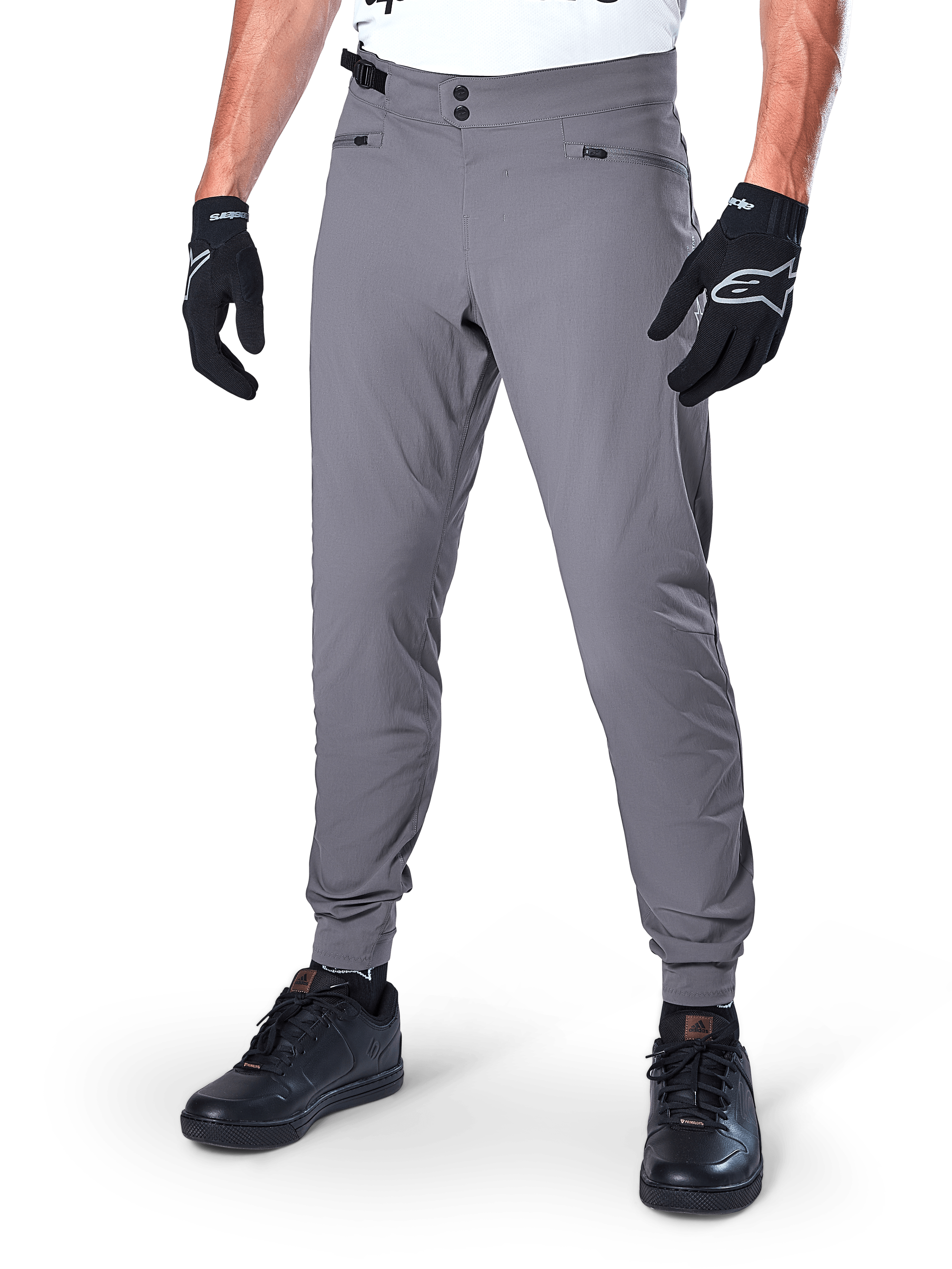 Calças Alpinestars A-Dura, calças de MTB cinzento escuro, com fecho de pressão duplo na cintura e bolsos com fecho de correr, punhos elásticos, usadas com luvas de ciclismo pretas e sapatilhas pretas