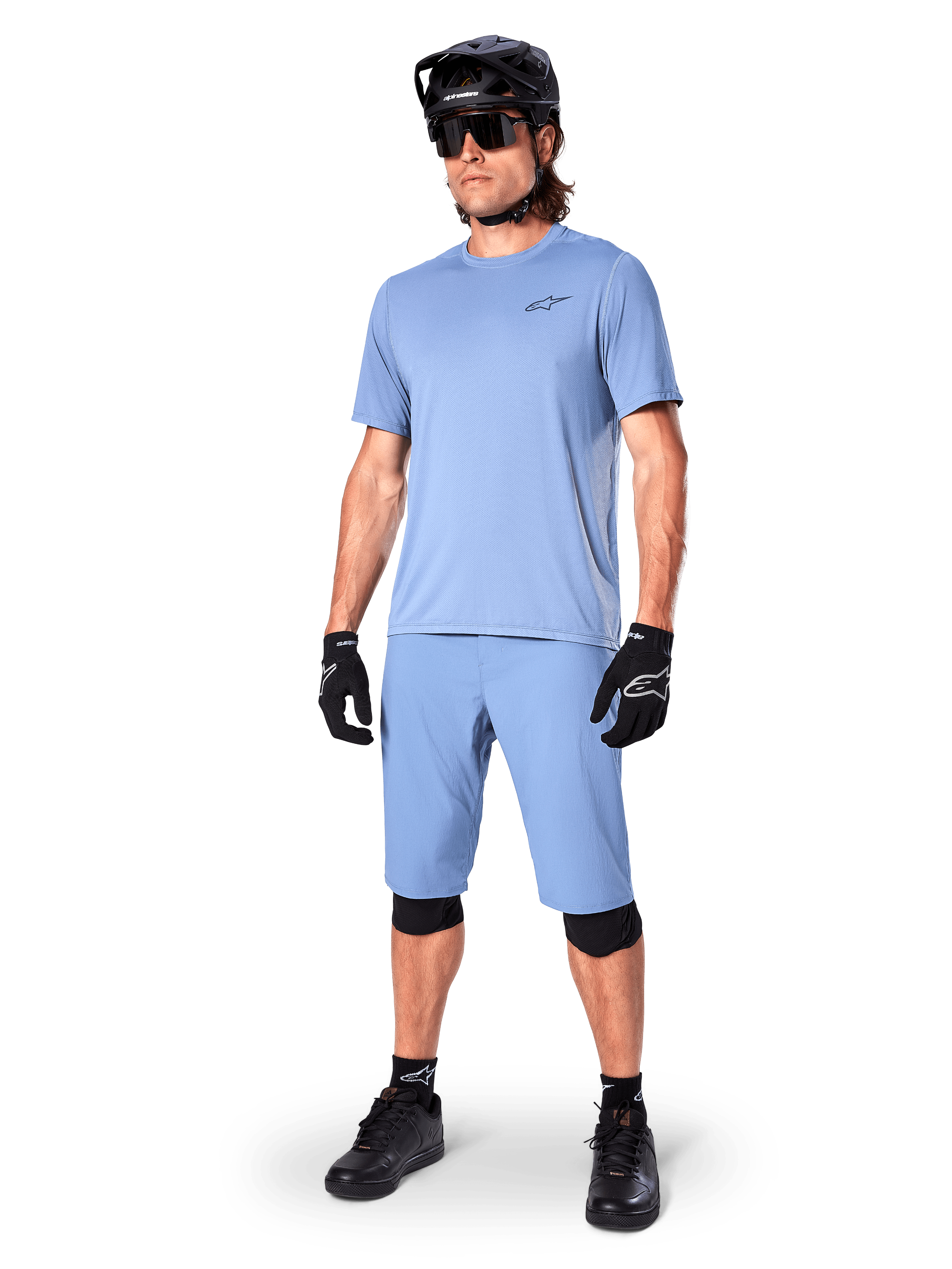Modelo a usar calções Alpinestars A-Dura em Infinity Blue, camisola de manga curta azul-claro a condizer, capacete de BTT preto, óculos de sol e luvas pretas, equipamento completo de BTT para trail
