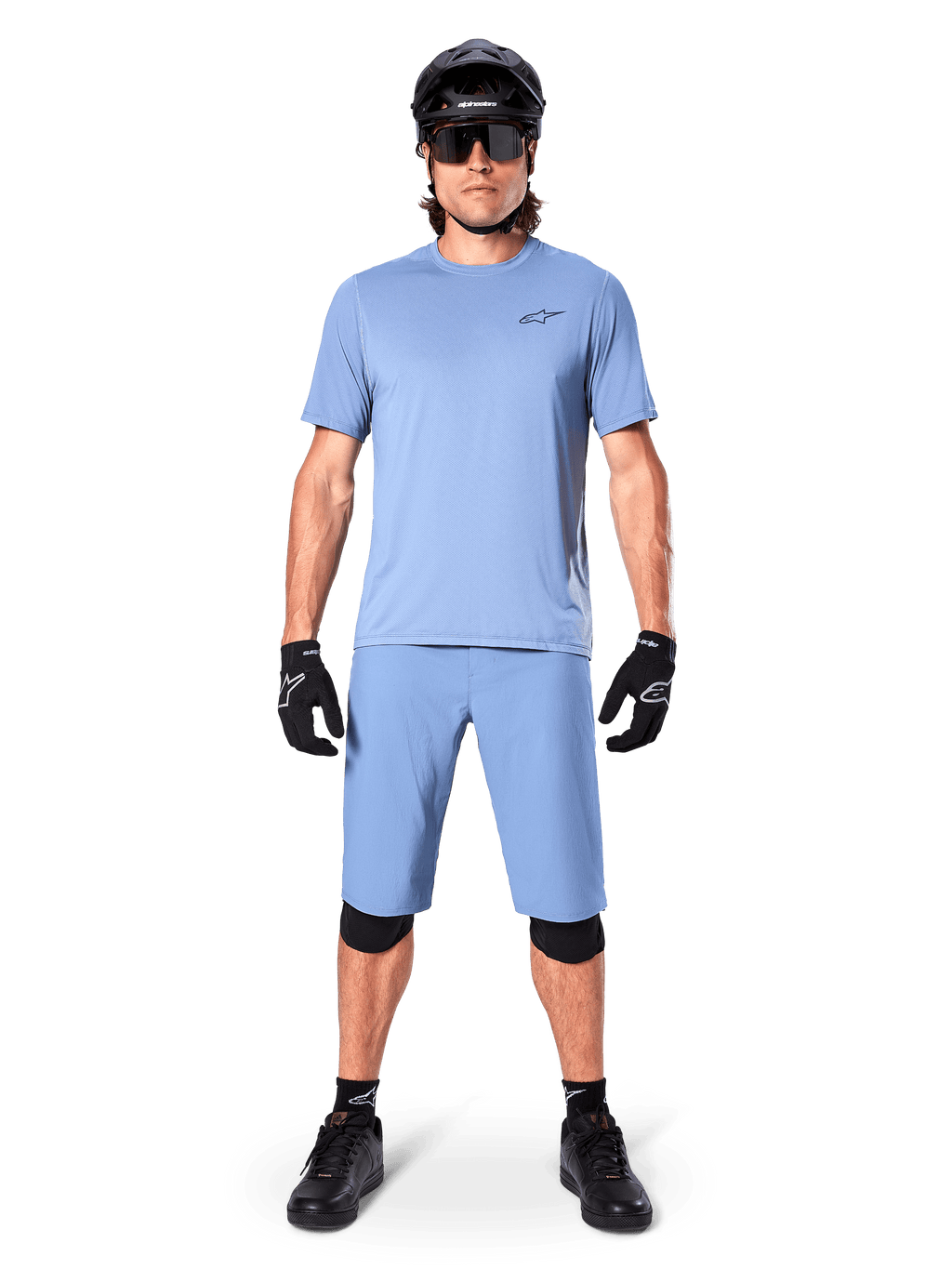 Modelo a usar calções Alpinestars A-Dura em Infinity Blue, camisola azul-claro a condizer, capacete de BTT preto, óculos de sol pretos, luvas e joelheiras pretas, equipamento completo de BTT para trail riding