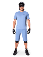 Modelo a usar calções Alpinestars A-Dura em Infinity Blue, camisola azul-claro a condizer, capacete de BTT preto, óculos de sol pretos, luvas e joelheiras pretas, equipamento completo de BTT para trail riding