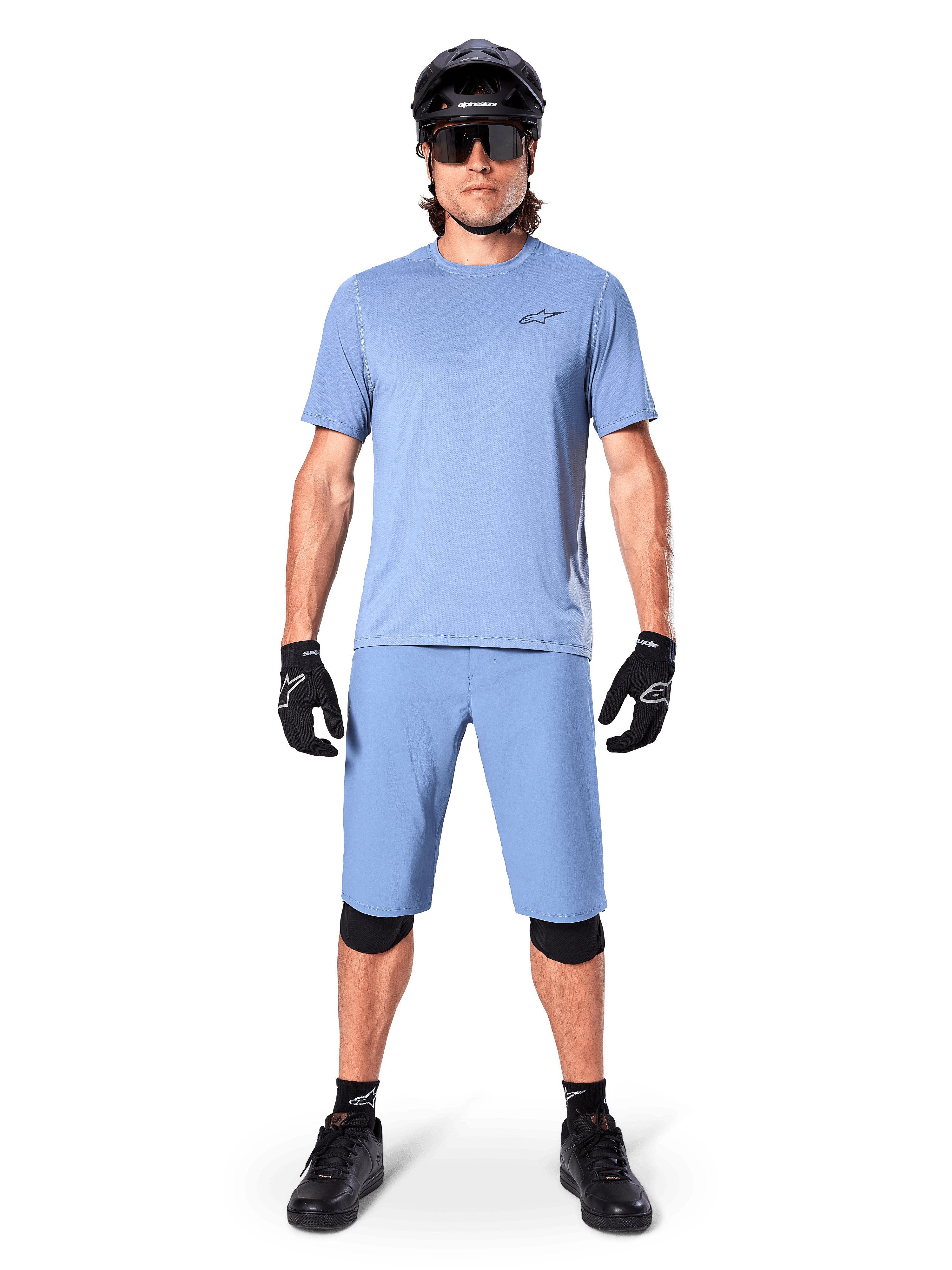 Modelo a usar calções Alpinestars A-Dura em Infinity Blue, camisola azul-claro a condizer, capacete de BTT preto, óculos de sol pretos, luvas e joelheiras pretas, equipamento completo de BTT para trail riding