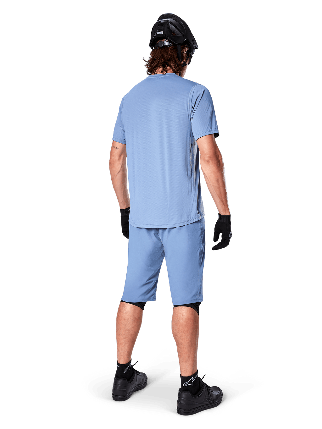 Vista traseira de um ciclista de montanha a usar calções Alpinestars A-Dura em Infinity Blue, camisola de manga curta a condizer, capacete preto, luvas pretas e sapatos pretos, equipamento de performance coordenado para trilhos de BTT