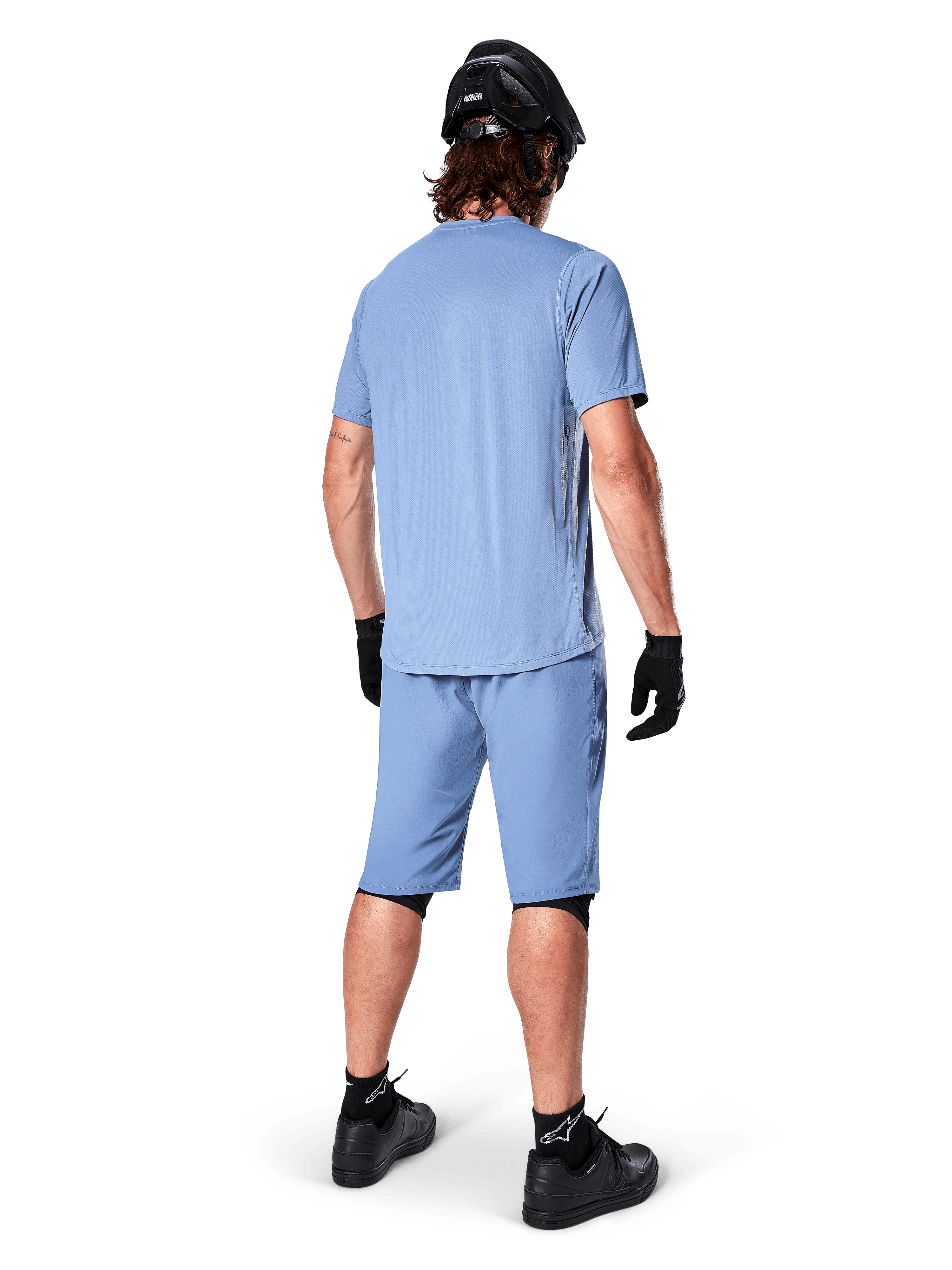 Vista traseira de um ciclista de montanha a usar calções Alpinestars A-Dura em Infinity Blue, camisola de manga curta a condizer, capacete preto, luvas pretas e sapatos pretos, equipamento de performance coordenado para trilhos de BTT