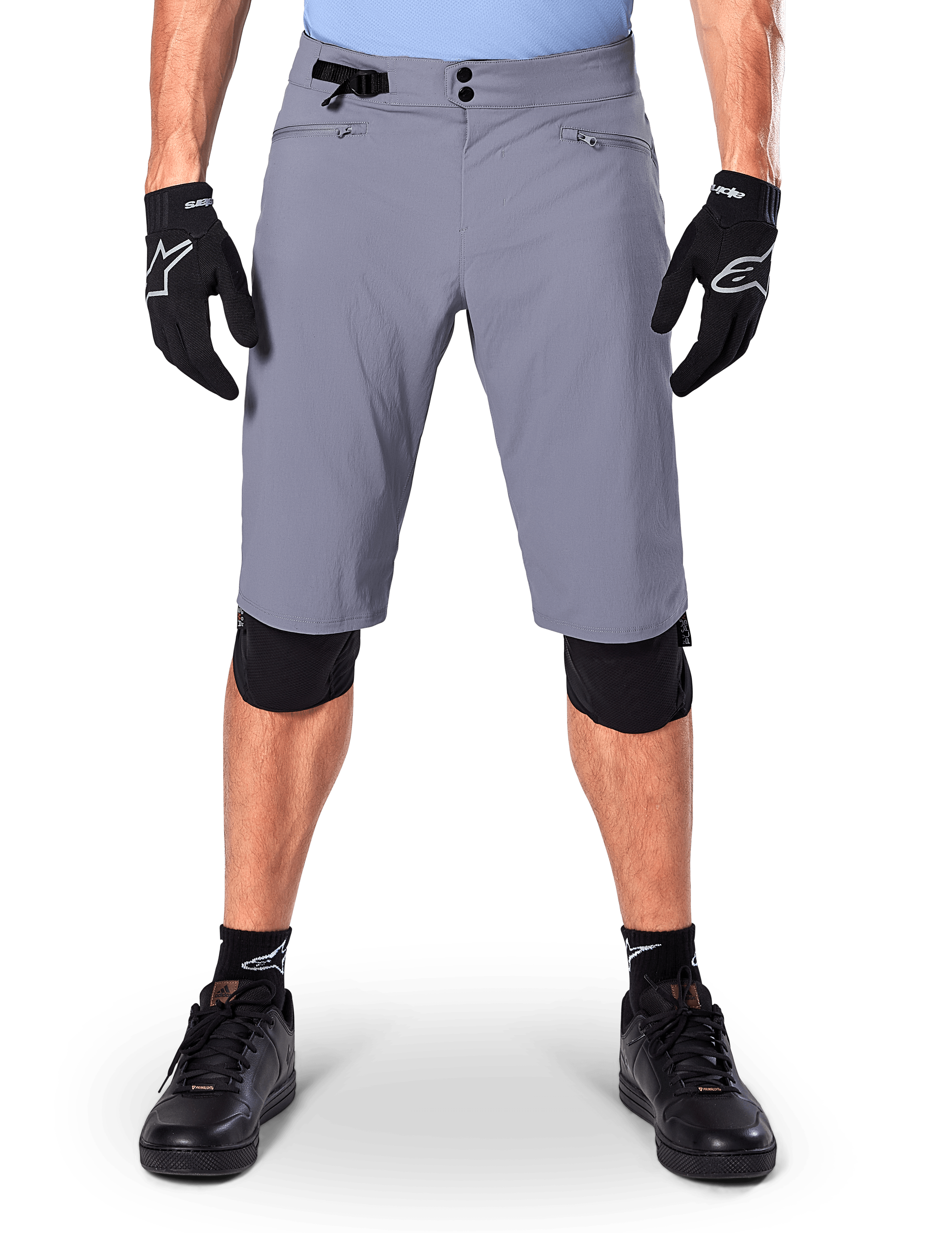 Calções Alpinestars A-Dura, calções de mountain bike, cinzento-escuro, usados com luvas e joelheiras pretas Alpinestars, com fecho duplo de pressão e bolsos com fecho e forro em rede, tecido durável com elasticidade bidirecional para ciclismo fora de estrada
