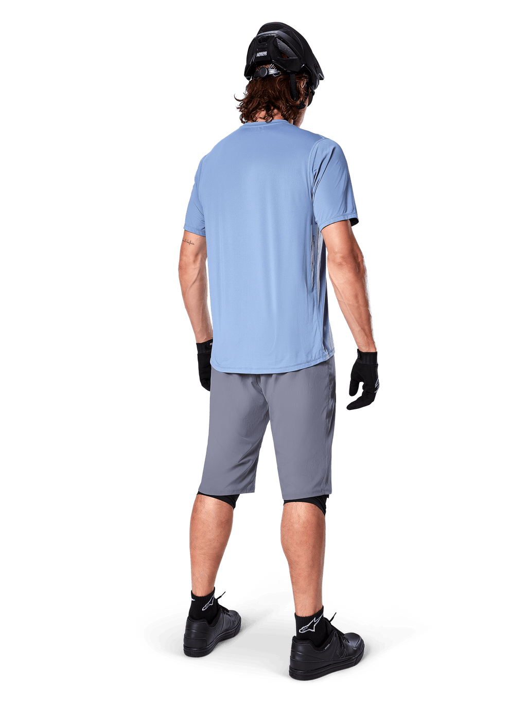 Calções Alpinestars A-Dura, calções de BTT cinzento escuro, vista traseira, usados com camisola de manga curta azul claro e capacete de BTT preto, luvas e meias pretas com sapatos pretos, equipamento funcional e durável para ciclismo todo-o-terreno