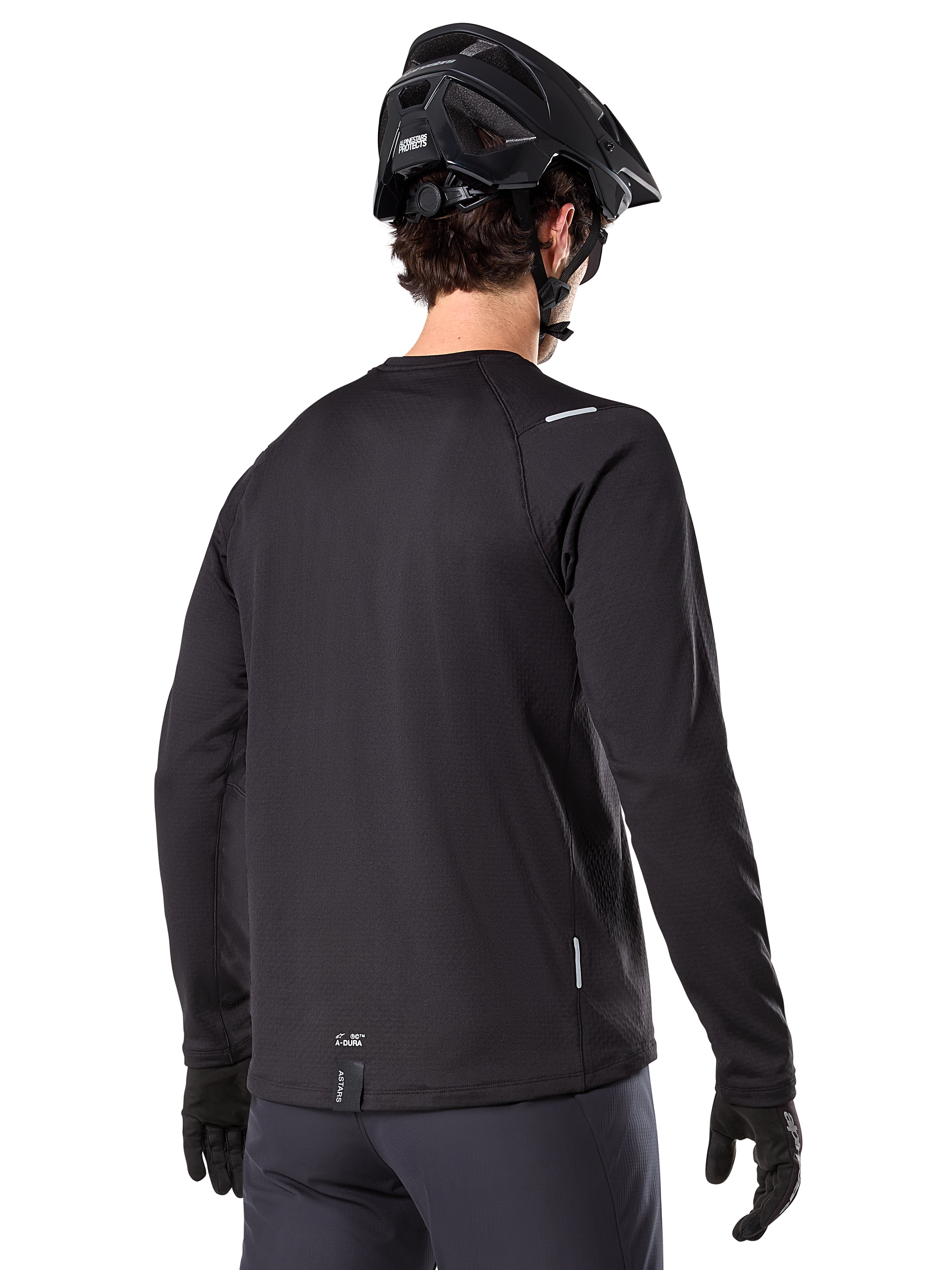 Alpinestars A-Dura Thermal Jersey, long-sleeve mountain bike jersey, Black, back view showing extended drop tail, small reflective details, and hem branding, worn with a black helmet and gloves for cold-weather cycling