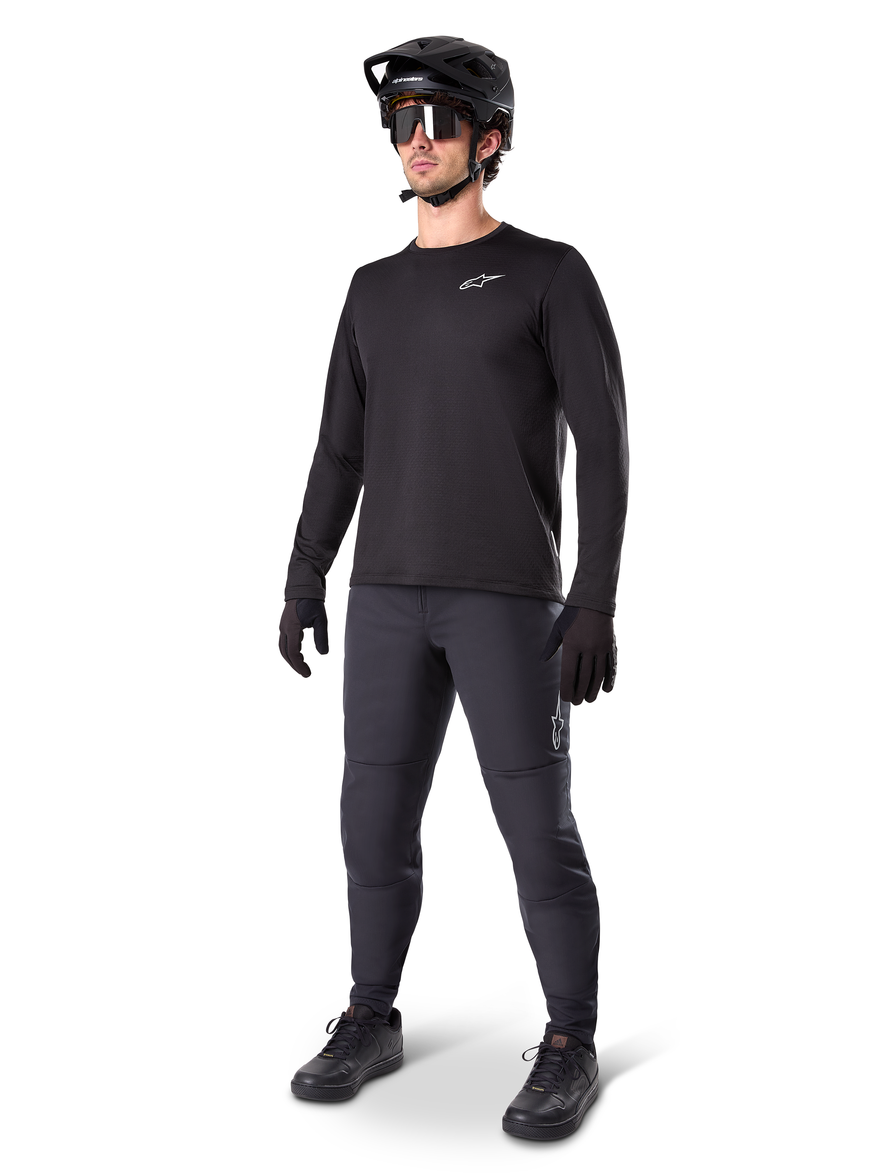 Model wearing Alpinestars A-Dura Thermal Jersey, Black long-sleeve MTB jersey, black mountain bike helmet, sunglasses, and dark grey pants, featuring a small white logo on the chest, insulated fleece construction for cold-weather riding