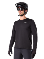 Alpinestars A-Dura Thermal Jersey, Black long-sleeve mountain bike jersey, white chest logo, worn with black helmet and gloves, sleek sporty design for trail riding