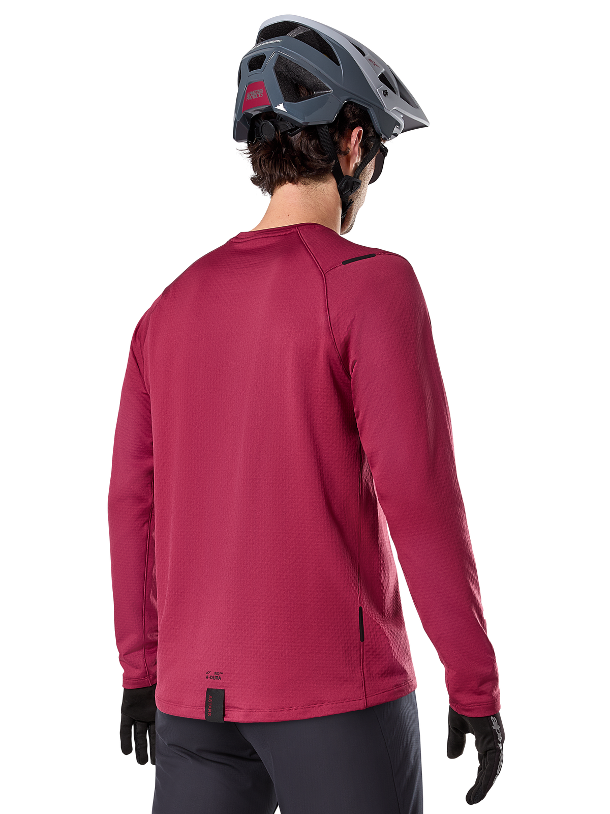 Alpinestars A-Dura Thermal Jersey, camisola de BTT de manga comprida, bordeaux, vista traseira num modelo com capacete de BTT cinzento e luvas pretas, com cauda traseira alongada e pequenos detalhes do logótipo, concebida para a prática de trilhos em climas frios.