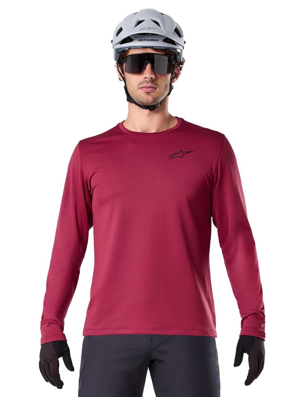 Ciclista masculino com Camisola Térmica Alpinestars A-Dura, camisola de BTT de manga comprida, cor bordô, combinada com capacete cinzento e óculos de sol pretos, apresenta um pequeno logótipo de estrela preto no peito, tecido de lã isolante para ciclismo de montanha em tempo frio