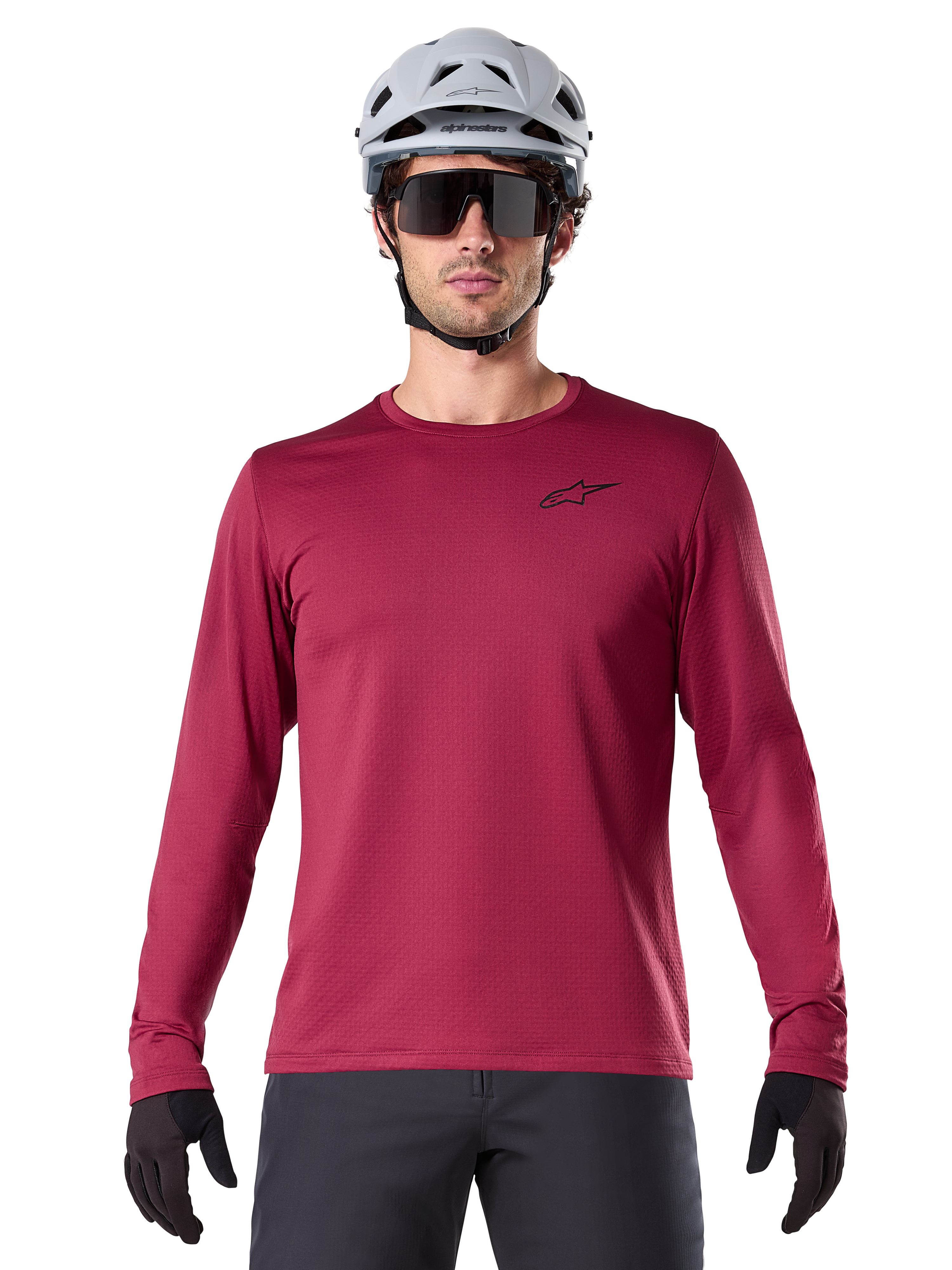 Ciclista masculino com Camisola Térmica Alpinestars A-Dura, camisola de BTT de manga comprida, cor bordô, combinada com capacete cinzento e óculos de sol pretos, apresenta um pequeno logótipo de estrela preto no peito, tecido de lã isolante para ciclismo de montanha em tempo frio