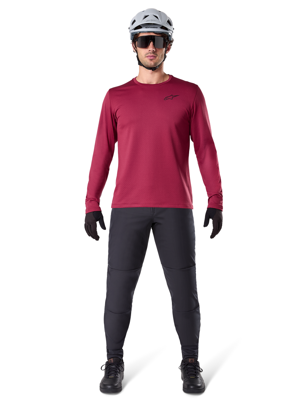 Modelo masculino a usar a Alpinestars A-Dura Thermal Jersey em Vermelho, camisola de ciclismo de manga comprida isolada, combinada com calças de BTT cinzento escuro, capacete branco, óculos de sol pretos e luvas pretas, equipamento profissional de BTT para tempo frio