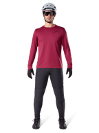 Modelo masculino a usar a Alpinestars A-Dura Thermal Jersey em Vermelho, camisola de ciclismo de manga comprida isolada, combinada com calças de BTT cinzento escuro, capacete branco, óculos de sol pretos e luvas pretas, equipamento profissional de BTT para tempo frio