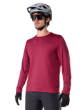 Alpinestars A-Dura Thermal Jersey, camisola de ciclismo de montanha de manga comprida, vermelho bordeaux, com forro de lã isolante e um pequeno logótipo preto no peito, usada com capacete cinzento, óculos de sol pretos e luvas pretas, concebida para ciclismo em tempo frio