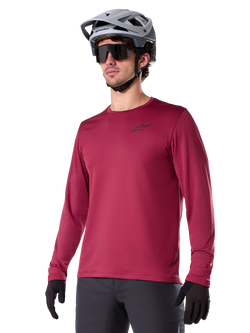 Alpinestars A-Dura Thermal Jersey, camisola de ciclismo de montanha de manga comprida, vermelho bordeaux, com forro de lã isolante e um pequeno logótipo preto no peito, usada com capacete cinzento, óculos de sol pretos e luvas pretas, concebida para ciclismo em tempo frio