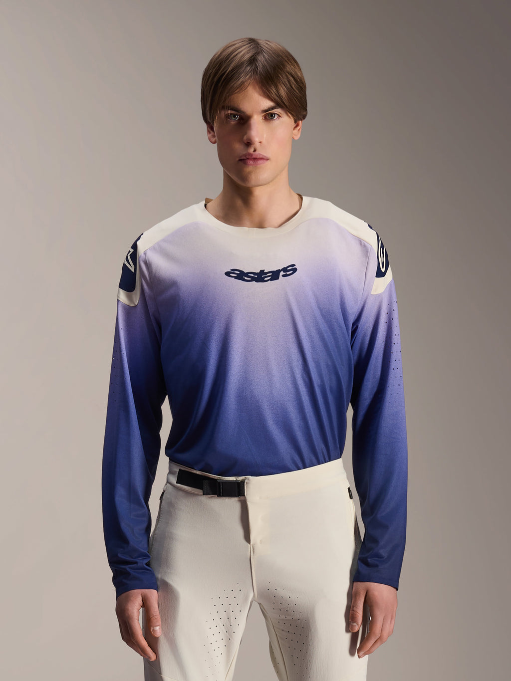 Alpinestars A-Aria Polartec Maker Elite Jersey, camisola de manga comprida para BTT, Baja Blue com gradiente de branco para azul, usada por um modelo com calças brancas, com logótipo azul escuro no peito e perfurações a laser nas mangas, vestuário de performance para ciclismo de montanha