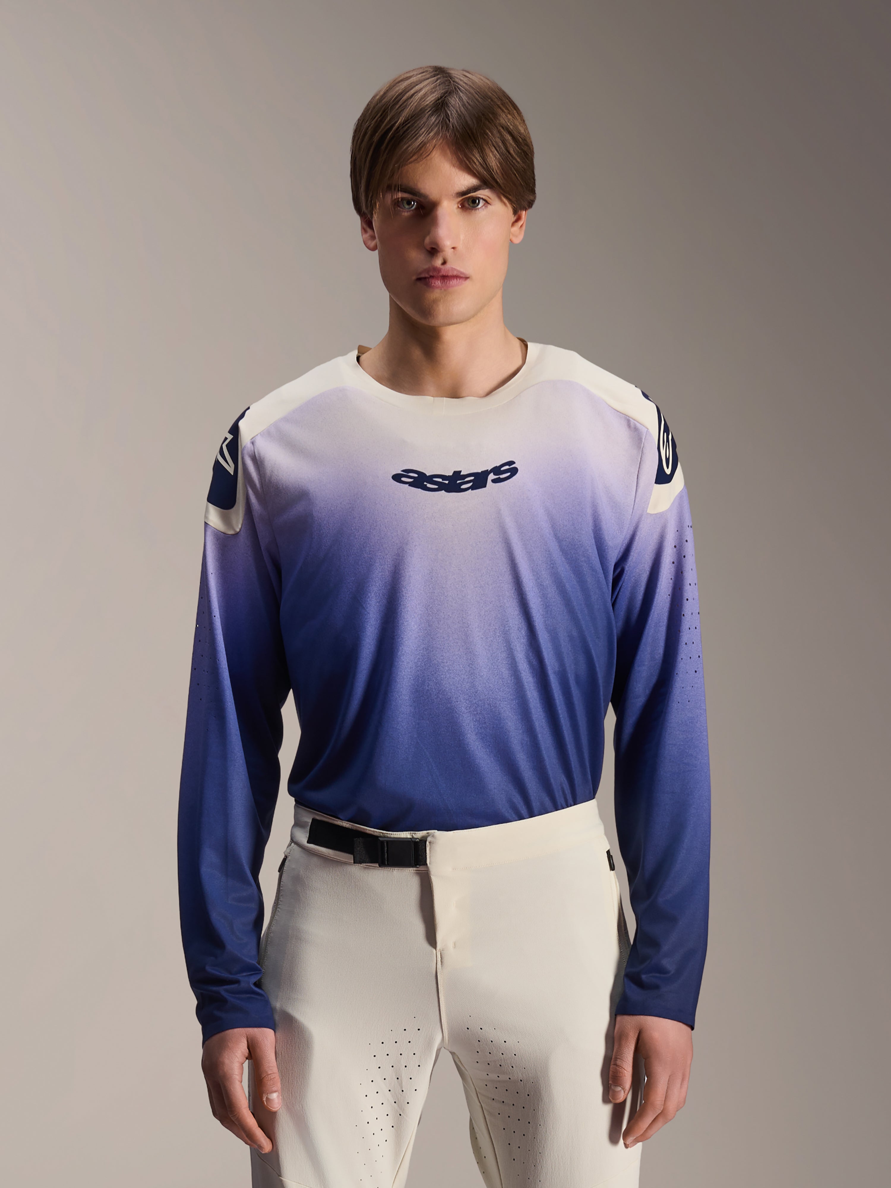 Alpinestars A-Aria Polartec Maker Elite Jersey, camisola de manga comprida para BTT, Baja Blue com gradiente de branco para azul, usada por um modelo com calças brancas, com logótipo azul escuro no peito e perfurações a laser nas mangas, vestuário de performance para ciclismo de montanha