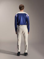 Calças Alpinestars A-Aria Elite em Ecru, vistas de trás num modelo combinadas com uma camisola de manga comprida azul A-Aria Polartec Maker Elite, calças técnicas de BTT em branco sujo com logótipos pretos na parte inferior das pernas, equipamento de ciclismo de performance para mountain biking