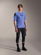 Modelo masculino a usar a camisola de manga curta Alpinestars A-Aria Polartec Elite em azul Baja Blue, combinada com calções de BTT pretos e joelheiras, com logótipos Astars pretos no peito e no ombro, equipamento de performance premium para BTT