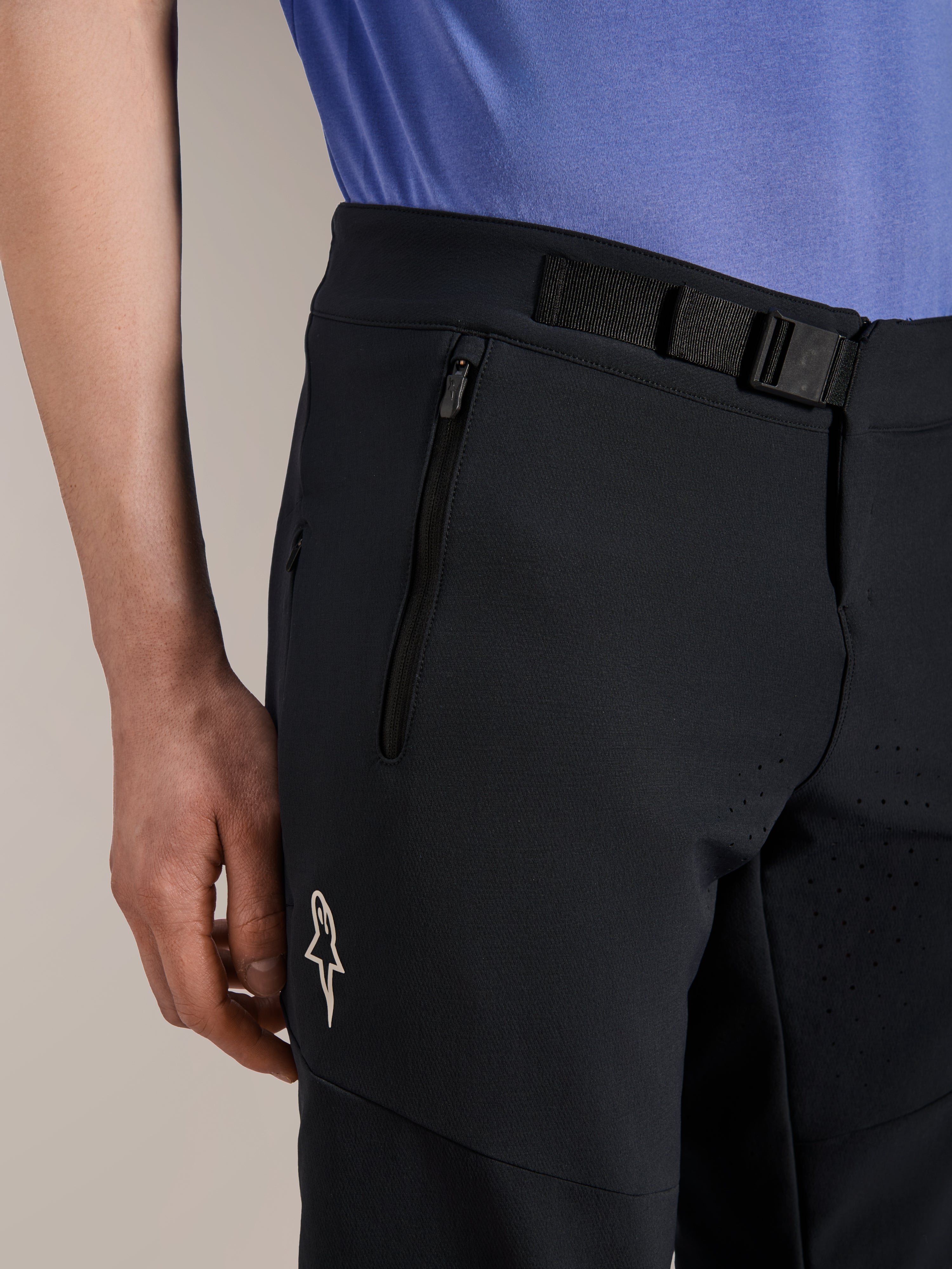 Alpinestars A-Aria Elite Shorts, calções de mountain bike, Black Titanium, com fecho de fivela magnética, bolso com fecho de correr e logótipo Alpinestars branco, usados com uma camisola de ciclismo azul, equipamento de performance para mountain bike