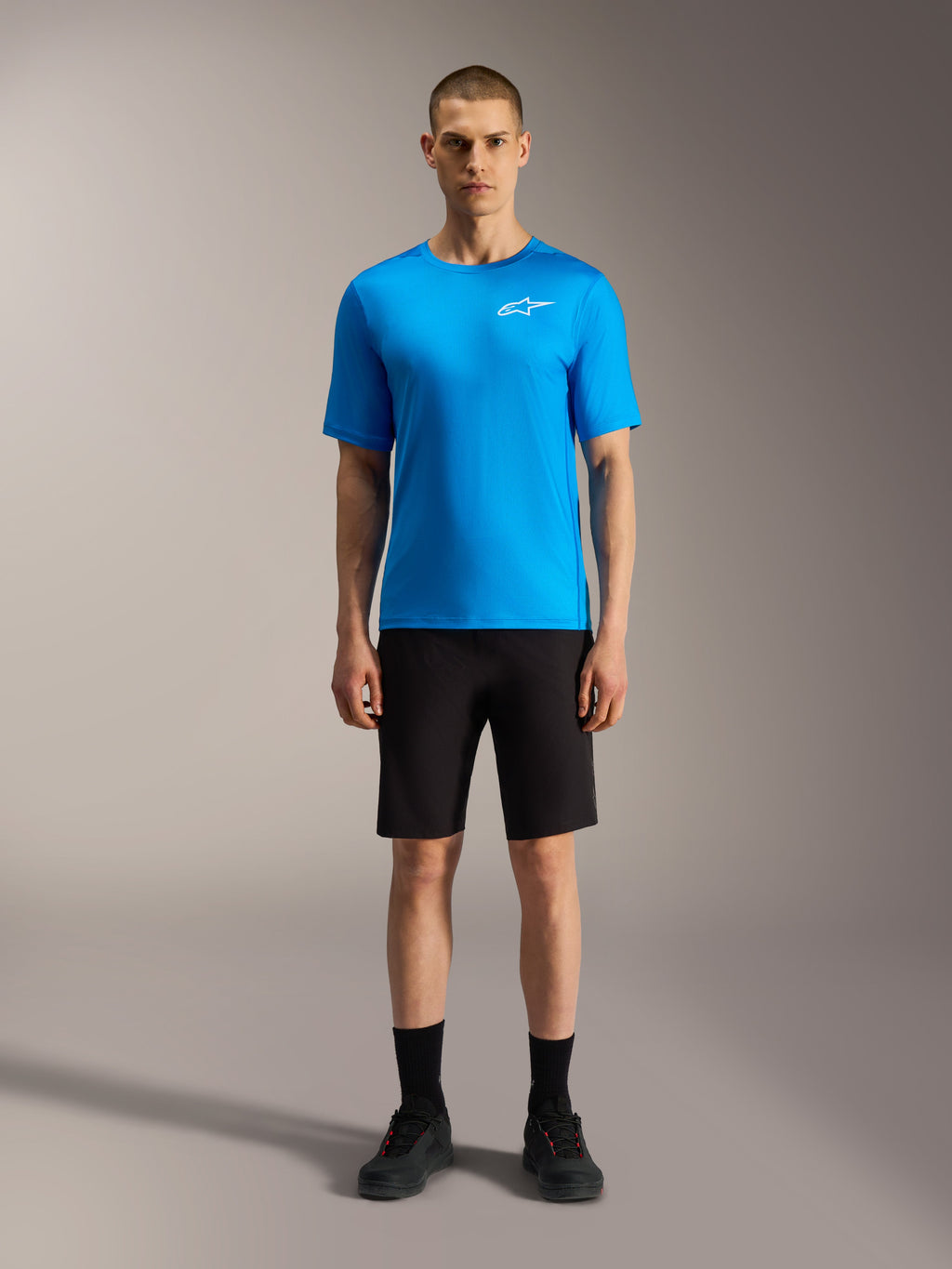 Alpinestars A-Dura Ride Shorts, calções pretos e camisola azul vibrante, equipamento de mountain bike num modelo.