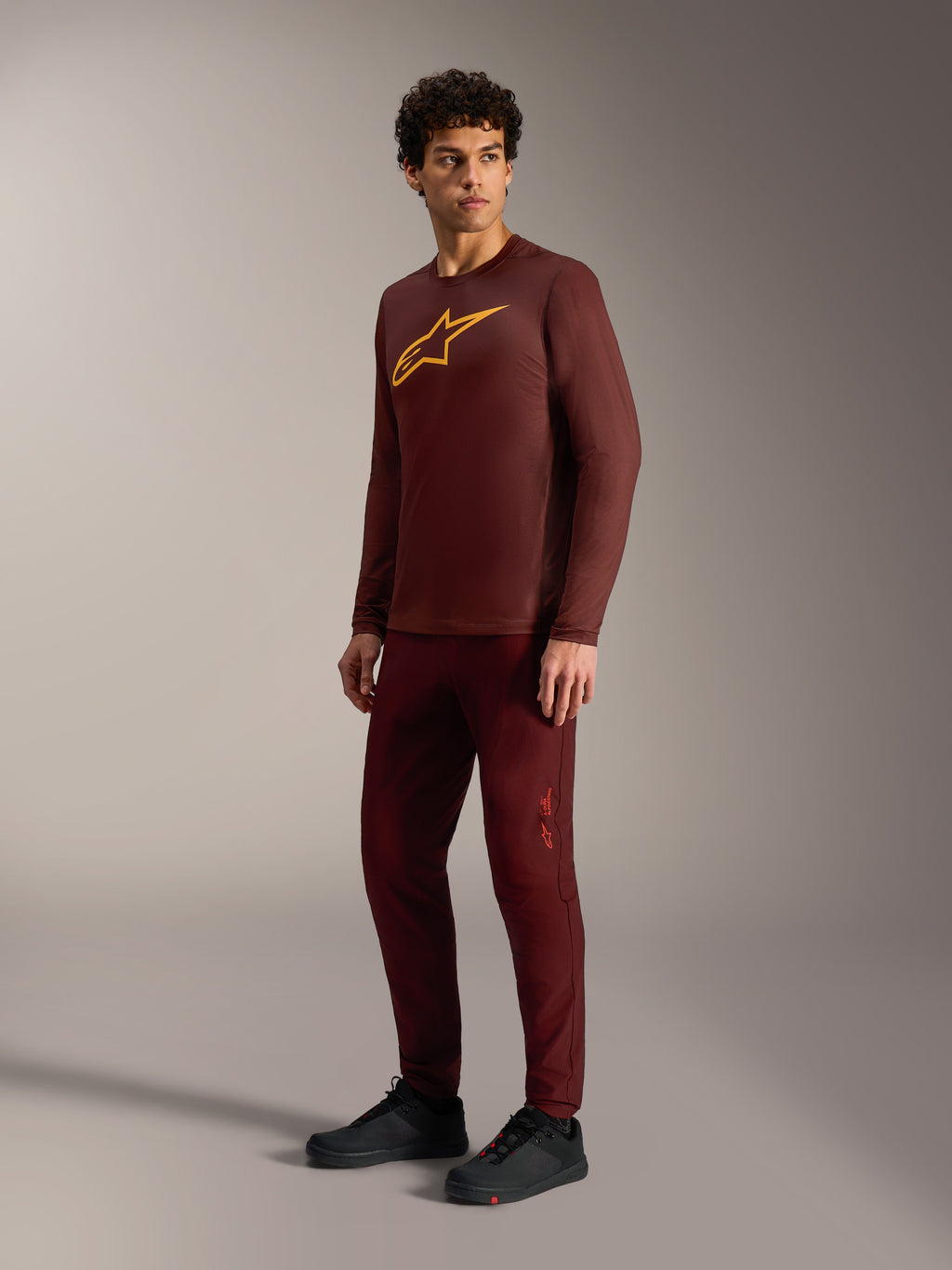 Camisola A-Dura Ride bordeaux de manga comprida, logótipo amarelo, calças a condizer e sapatilhas de ciclismo pretas.