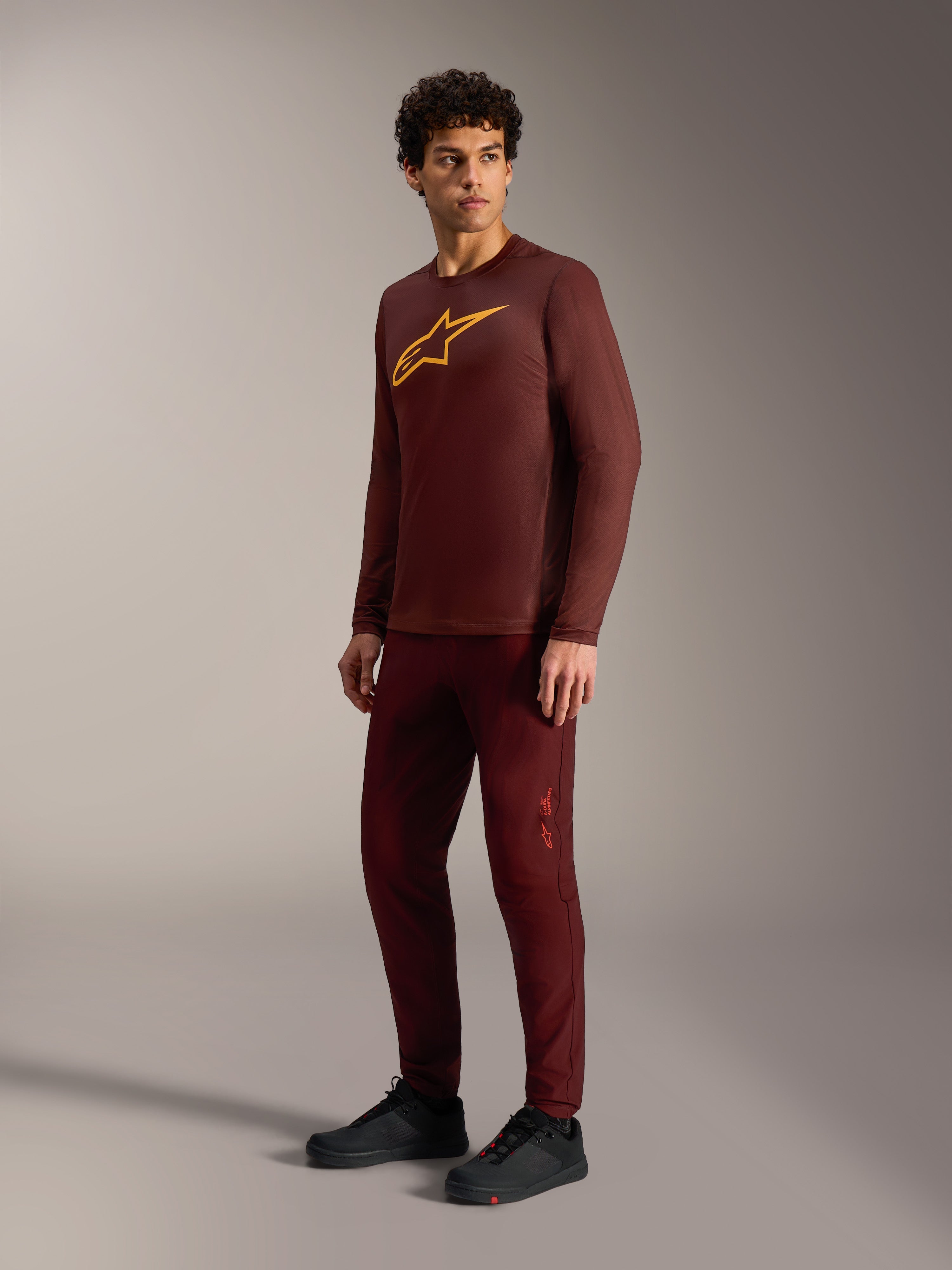 Camisola A-Dura Ride bordeaux de manga comprida, logótipo amarelo, calças a condizer e sapatilhas de ciclismo pretas.