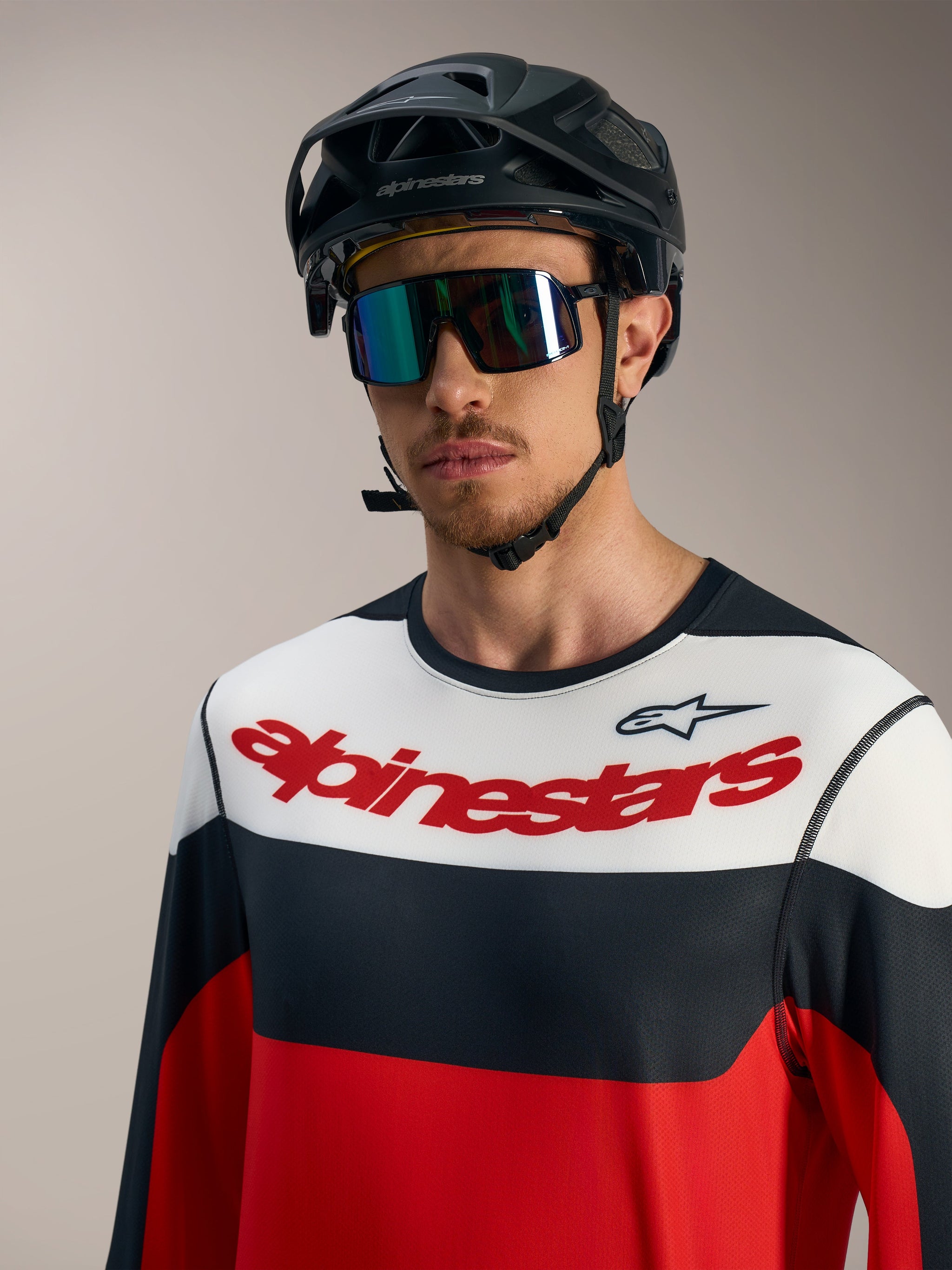 Camisola Alpinestars A-Dura Race vermelha, preta e branca com logótipo, capacete de BTT preto e óculos de proteção.
