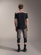 Camisola Alpinestars A-Dura Lipan - Manga Curta, preta com painel superior traseiro bege, vista traseira mostrando a cauda mais longa, usada com calções de BTT cinzentos e joelheiras pretas, vestuário de performance para bicicleta de montanha