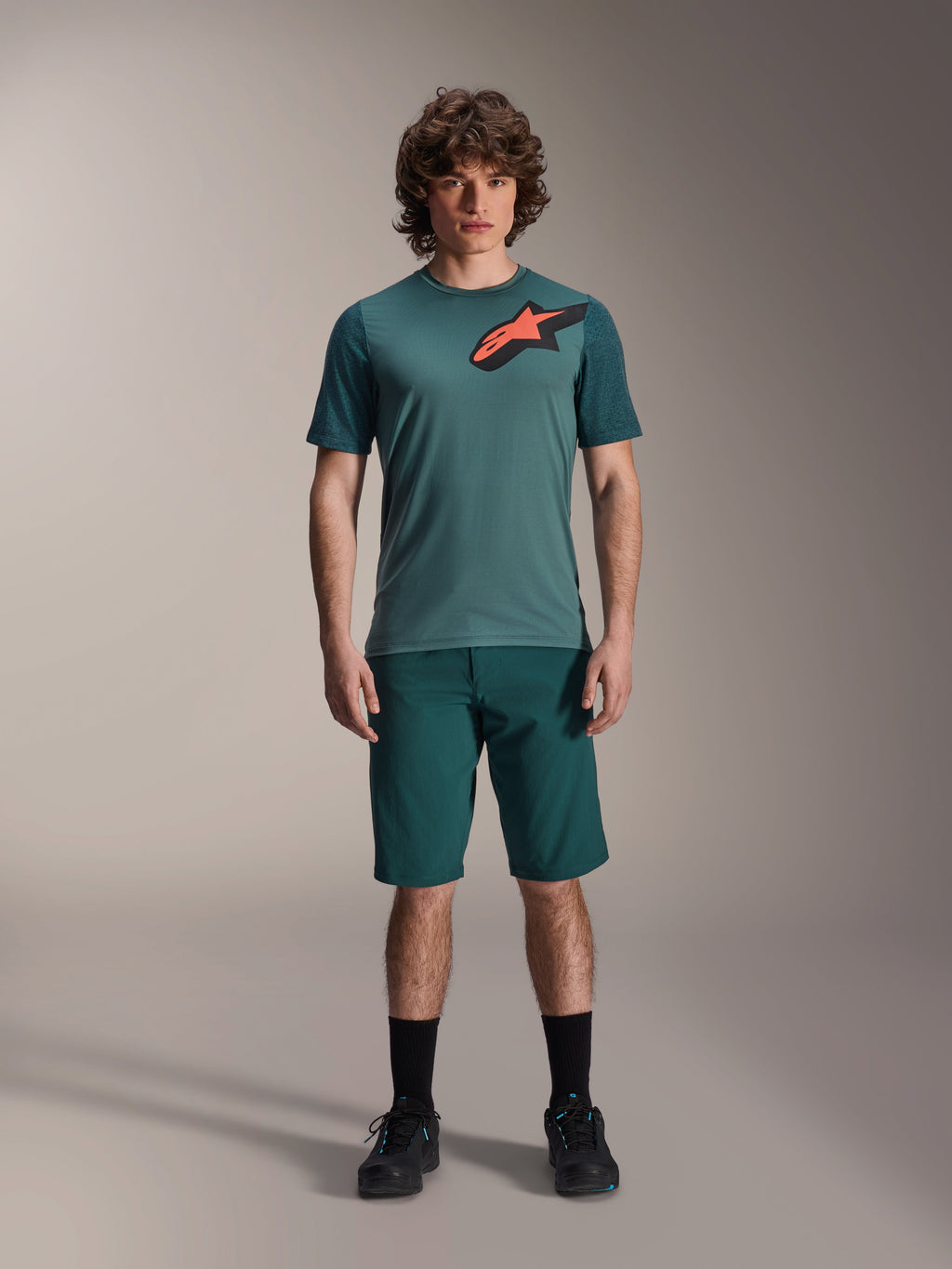Camisola Alpinestars A-Dura Lipan, camisola de BTT de manga curta, verde Silver Pine com logótipo Astars em preto e laranja no peito, combinada com calções a condizer e calçado preto, equipamento técnico de BTT