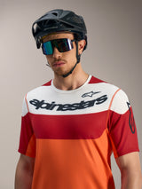 Alpinestars A-Dura Race Jersey in orange, red, and white with bold logos, paired with a black MTB helmet and sunglasses.