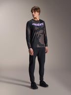 Modelo masculino a usar a Camisola de Manga Comprida Alpinestars A-Dura Hollow Camo, padrão Black Camo com gráfico 'astars' roxo no peito, combinada com calças técnicas pretas e sapatos pretos, equipamento casual de BTT