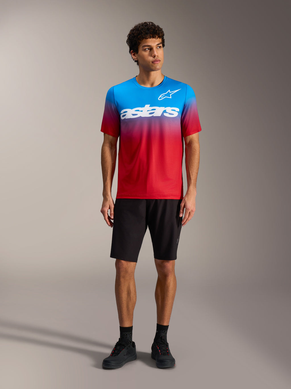Camisola A-Dura ASTARS 2.0 em gradiente vermelho e azul, logótipo branco, calções de BTT e sapatos pretos.