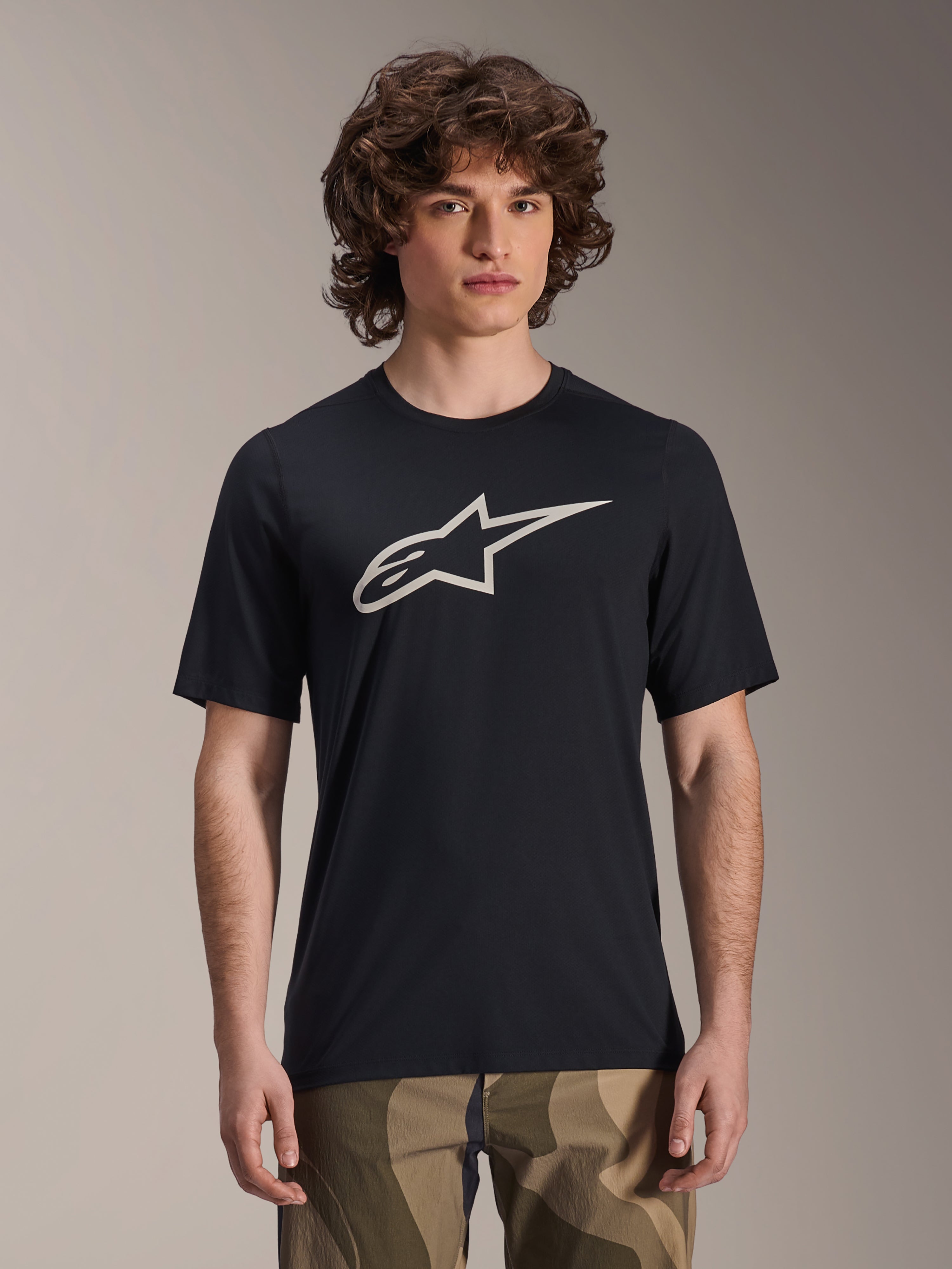 Alpinestars A-Dura Astar Jersey, camisola de BTT de manga curta, preta com logótipo de estrela branco, usada com calças camufladas, vestuário casual de BTT, tecido técnico que absorve a humidade