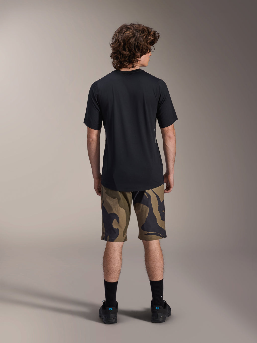 Camisola de Manga Curta Alpinestars A-Dura Astar, preta, vista traseira num modelo combinada com calções de BTT com padrão camuflado e calçado preto, vestuário técnico casual de mountain bike