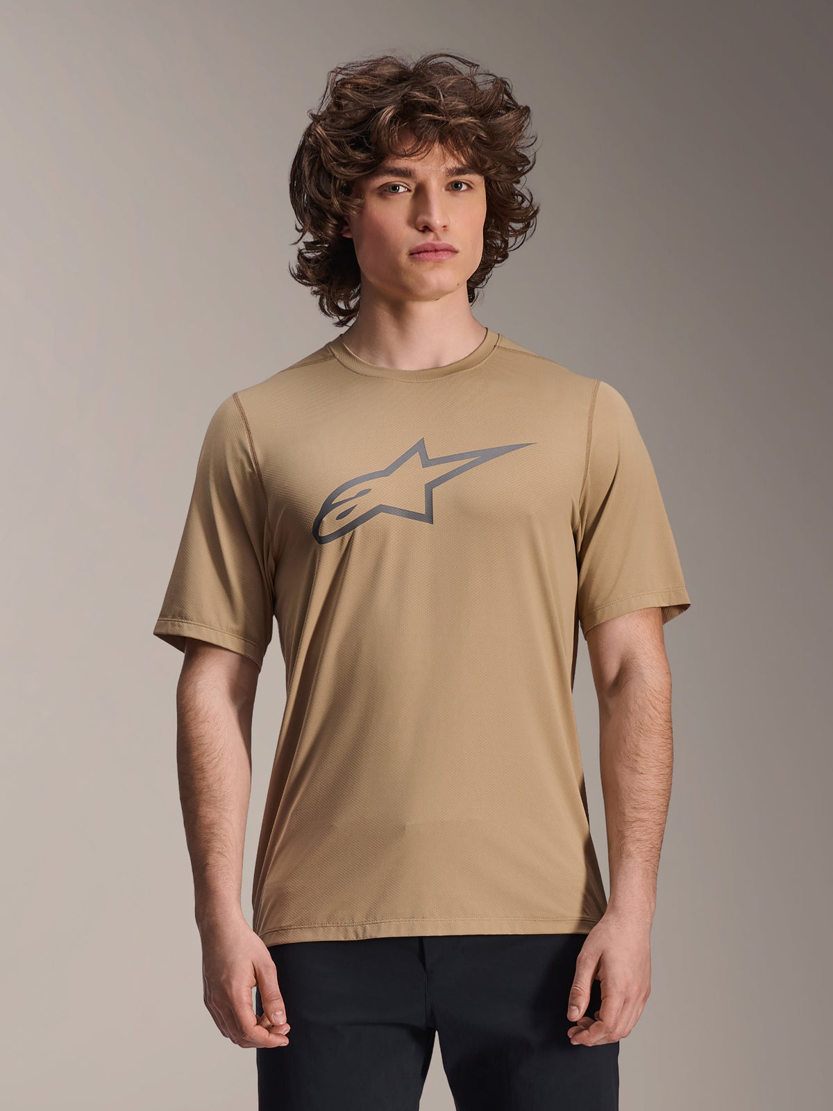 Alpinestars A-Dura Astar Jersey de manga curta, castanho claro, vestido por modelo masculino com calças pretas, logótipo de estrela Alpinestars cinzento no peito, jersey casual de mountain bike para trilhos