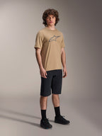 Alpinestars A-Dura Astar Short Sleeve Jersey, Light Brown, featuring a large dark gray Astar logo on the chest, worn by a model with black MTB shorts, black socks and black shoes, casual performance mountain bike apparel in a studio setting