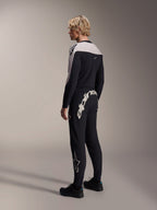 Calças Alpinestars A-Supra Melt, calças de MTB, pretas, com um grande logótipo Alpinestars branco na pala traseira e logótipo de estrela na perna, usadas por um modelo com uma camisola de manga comprida a condizer e sapatos pretos, vista lateral traseira