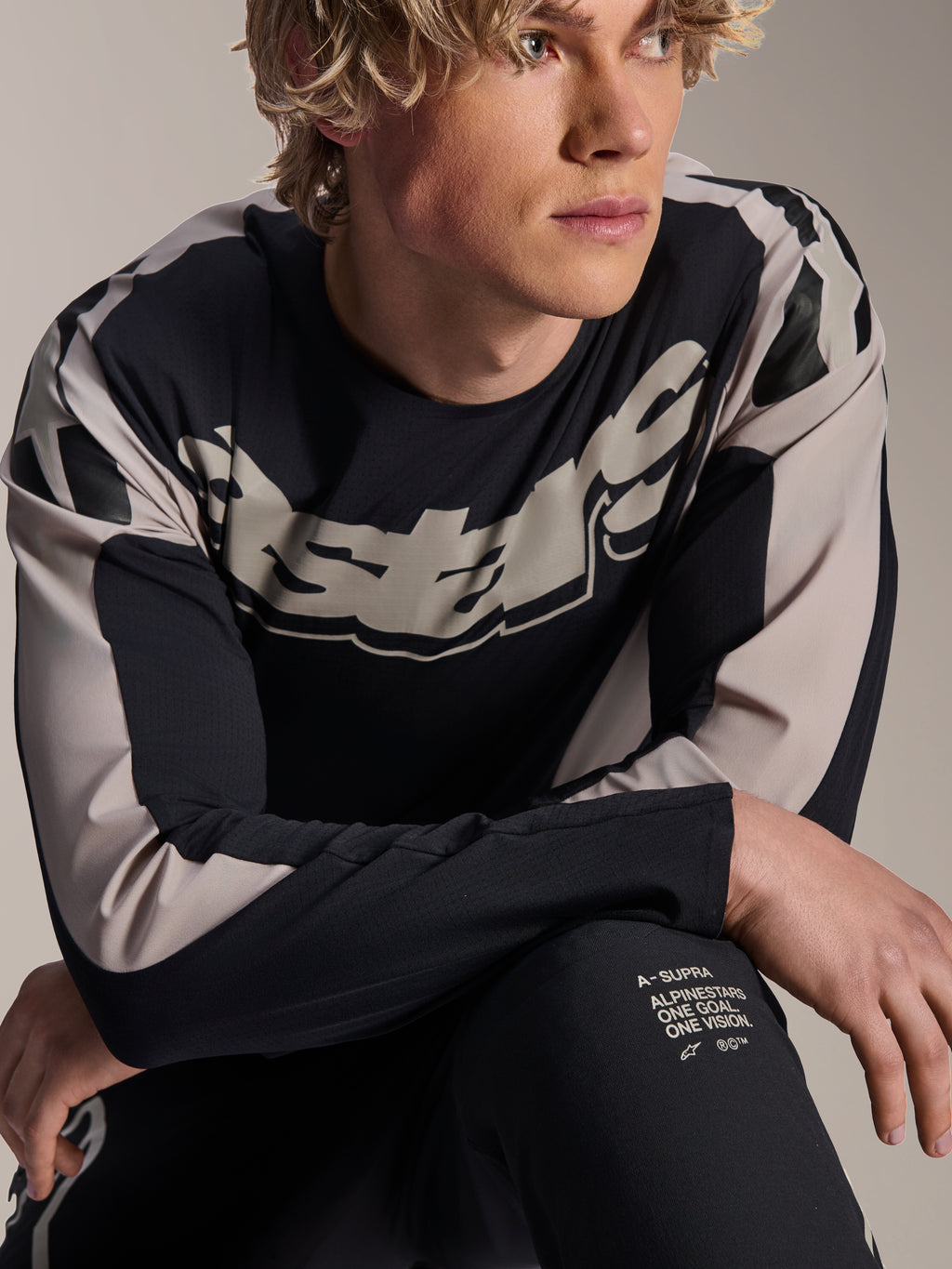 Alpinestars A-Supra Melt Jersey, camisola de BTT de manga comprida, preta com grafismos cinzento-claro, usada por modelo, com logótipo de destaque no peito e branding 'One Goal. One Vision.', vestuário de performance para BTT