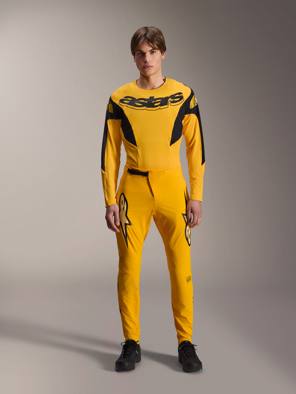 Conjunto de Equipamento Limited Edition A-Supra Melt Gold, roupa de BTT Alpinestars, amarelo escuro e preto, modelo a usar camisola de manga comprida com logótipo 'astars' arrojado no peito e calças de performance a condizer, com ventilação cortada a laser na parte interna das coxas e fecho de catraca seguro na cintura, kit de corrida profissional de BTT