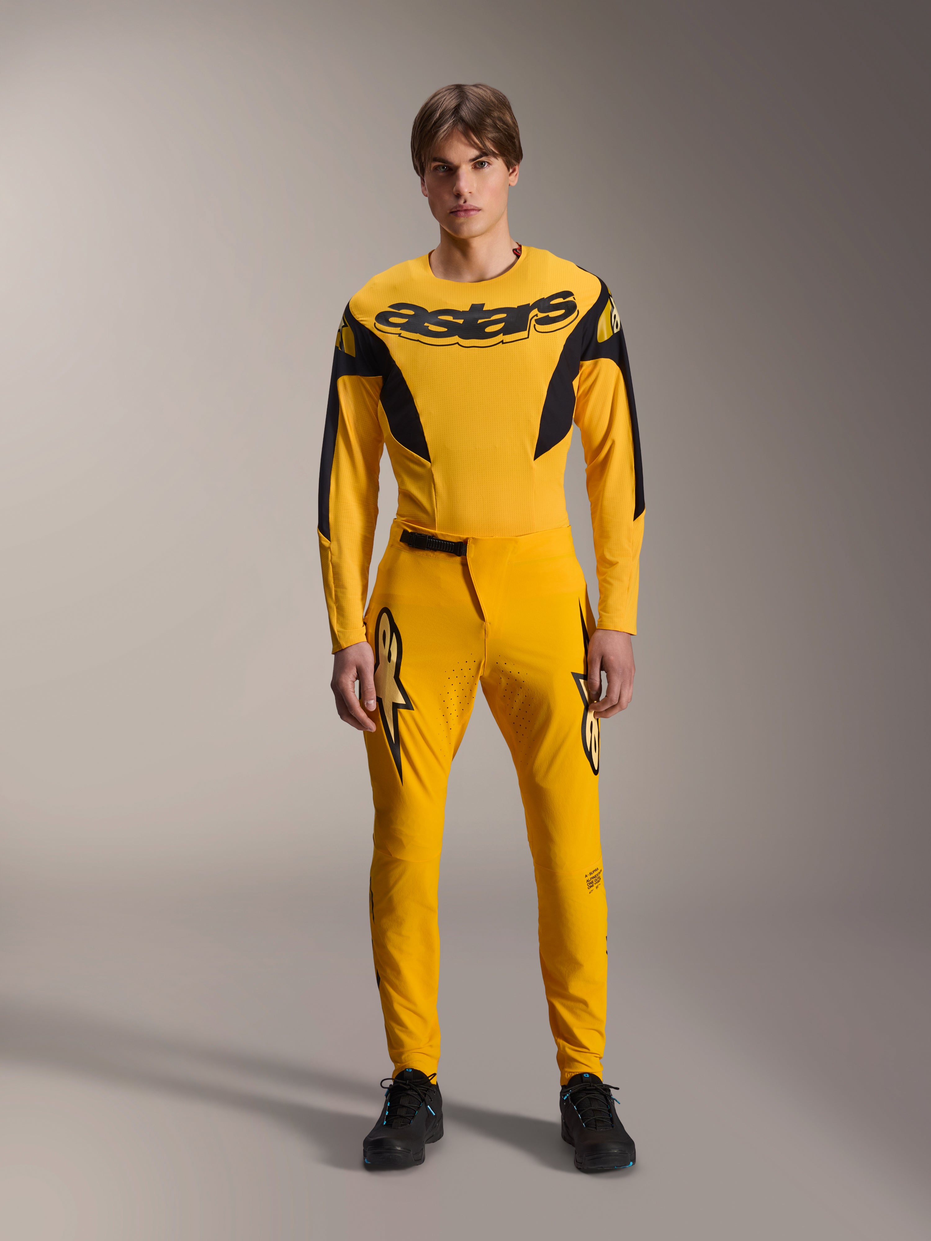 Conjunto de Equipamento Limited Edition A-Supra Melt Gold, roupa de BTT Alpinestars, amarelo escuro e preto, modelo a usar camisola de manga comprida com logótipo 'astars' arrojado no peito e calças de performance a condizer, com ventilação cortada a laser na parte interna das coxas e fecho de catraca seguro na cintura, kit de corrida profissional de BTT