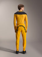 Vista traseira de um modelo a usar o conjunto de equipamento Alpinestars Limited Edition A-Supra Melt Gold, com uma camisola de manga comprida amarelo escuro com encaixe preto nos ombros e calças amarelo escuro a condizer com um grande logótipo Alpinestars na pala traseira, combinado com sapatos pretos.