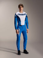 Modelo a usar equipamento de corrida MTB Alpinestars completo, camisola de manga comprida azul e branca com a marca 'astars', calças A-Supra Melt azuis a condizer com logótipos de estrela brancos, vestuário profissional de mountain bike para todo-o-terreno