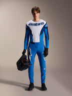 Modelo masculino com o equipamento de BTT Alpinestars A-Supra Melt, camisola de manga comprida branca e azul com a inscrição "astars", calças A-Supra Melt azuis com logótipo branco, capacete integral preto, luvas e sapatos pretos, conjunto de ciclismo todo-o-terreno coordenado