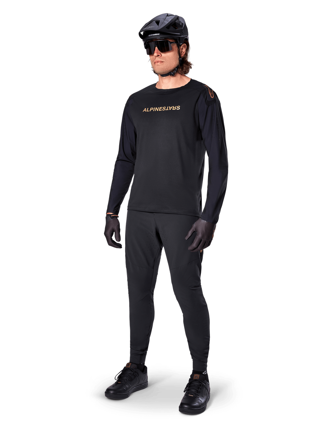 Alpinestars A-Aria Polartec Switch Long Sleeve Jersey, preta, logótipo em bronze no peito, usada por ciclista de montanha com capacete e óculos de sol pretos, vestuário de ciclismo de alta performance para trilhos