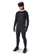 Alpinestars A-Aria Polartec Switch Long Sleeve Jersey, preta, logótipo em bronze no peito, usada por ciclista de montanha com capacete e óculos de sol pretos, vestuário de ciclismo de alta performance para trilhos