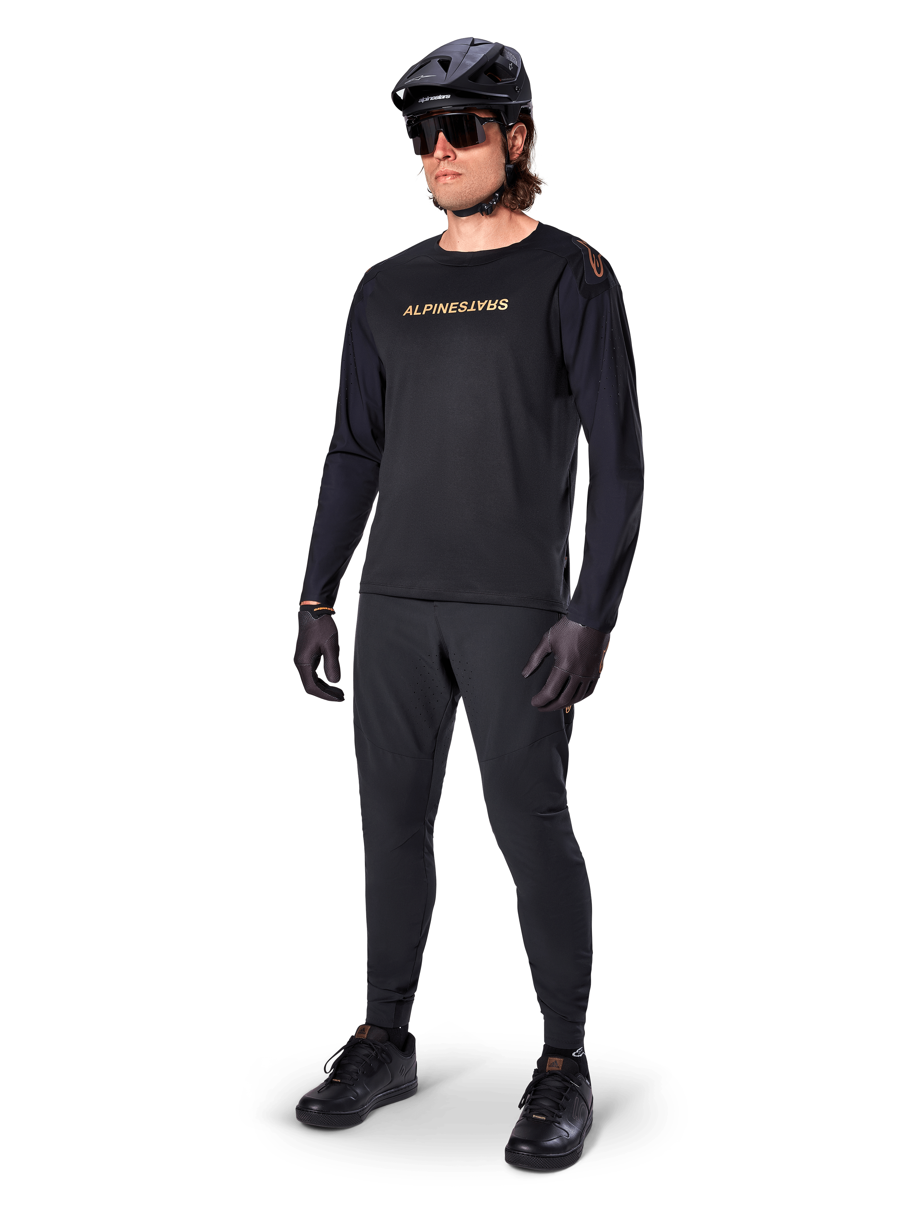 Alpinestars A-Aria Polartec Switch Long Sleeve Jersey, preta, logótipo em bronze no peito, usada por ciclista de montanha com capacete e óculos de sol pretos, vestuário de ciclismo de alta performance para trilhos